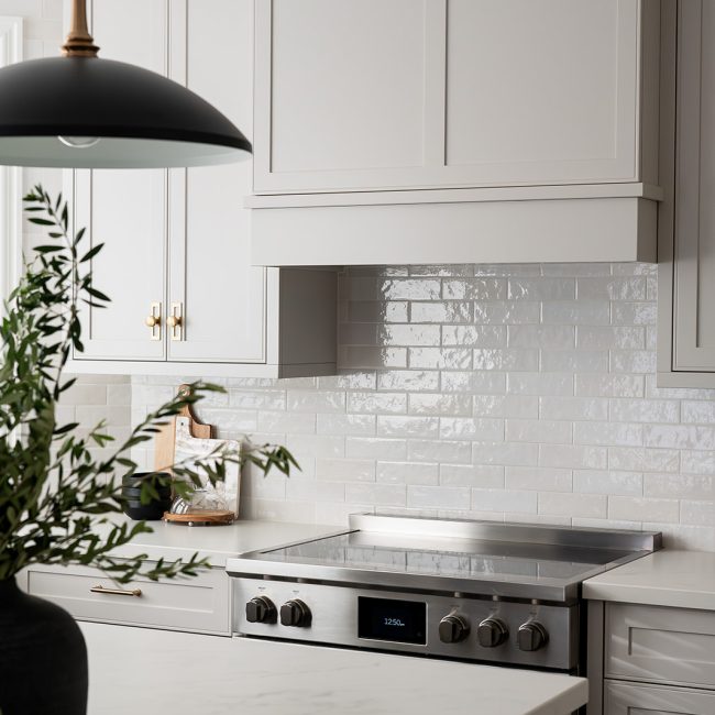 WIHM Design kitchen with white tile backsplash, white cabinets and brushed steel stove